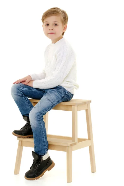 Um menino está sentado em uma cadeira . — Fotografia de Stock