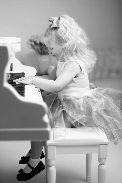 Menina bonita está tocando em um piano de cauda branco. — Fotografia de Stock