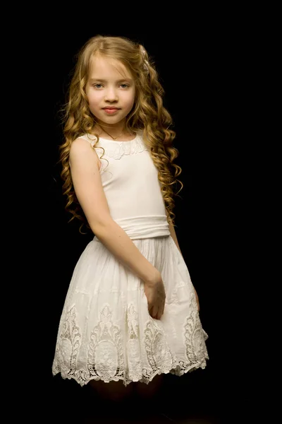 Ein kleines Mädchen kniet auf schwarzem Hintergrund im Studio. — Stockfoto