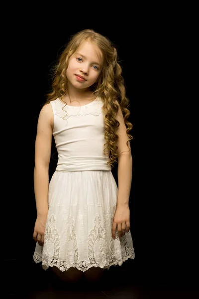 Uma menina está ajoelhada em um fundo preto no estúdio. — Fotografia de Stock