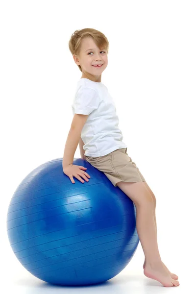 Der kleine Junge auf dem großen Ball übt sich in Fitness. weiße T-Shirts — Stockfoto
