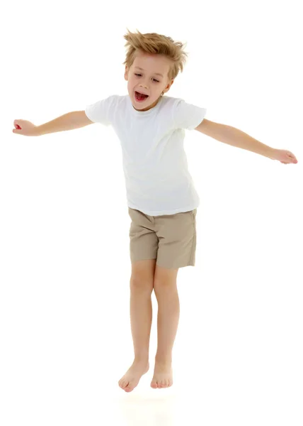 En liten pojke i en ren vit T-shirt hoppande roligt. Royaltyfria Stockbilder