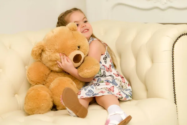 Little girl on sofa hugging teddy bear.