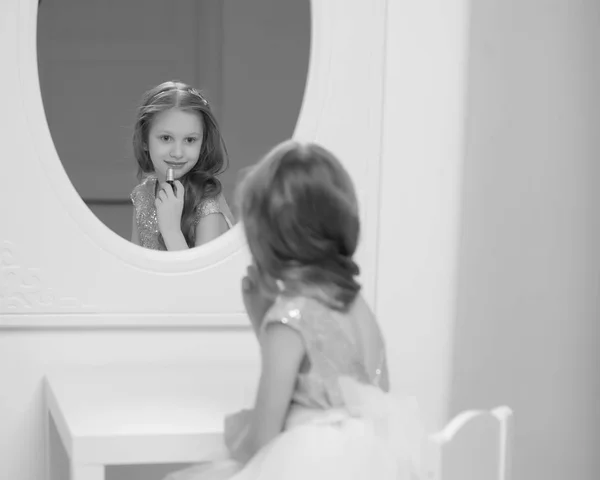 A little girl near the mirror paints lipstick lips — Stock Photo, Image