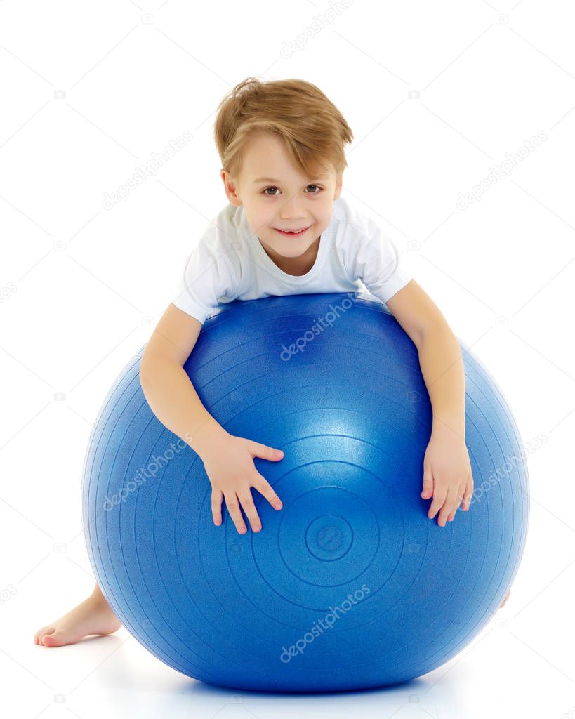 The little boy on the big ball is engaged in fitness. White T-sh