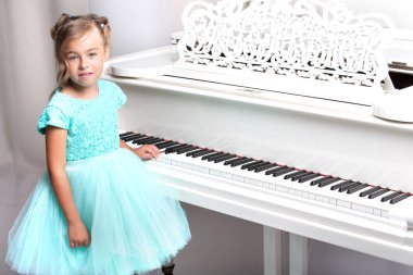 Güzel küçük kız beyaz bir piyanoda çalıyor..