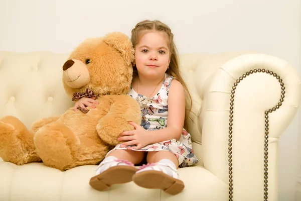 Niña en el sofá abrazando oso de peluche. —  Fotos de Stock