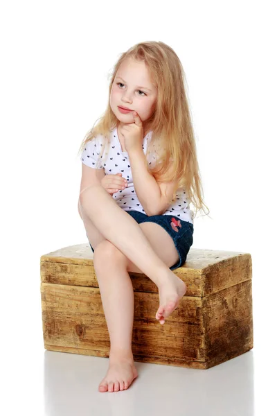 Une petite fille est assise sur une boîte en bois. — Photo