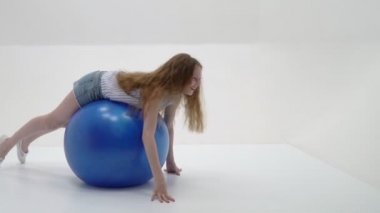 Küçük kız spor yapmak için büyük bir top üzerinde egzersiz yapıyor..