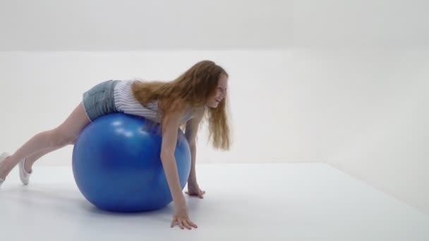 Klein meisje doet oefeningen op een grote bal voor fitness. — Stockvideo