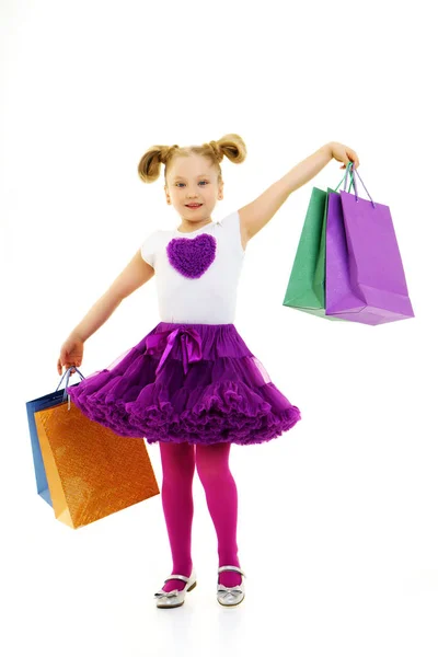 Liten flicka med flerfärgade väskor i sina händer. — Stockfoto