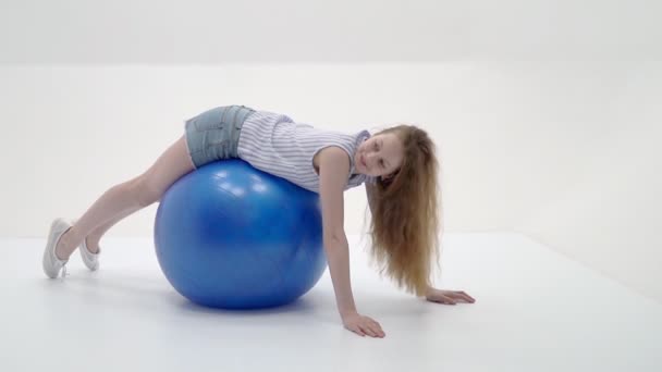 Kleines Mädchen macht Übungen auf einem großen Ball für Fitness. — Stockvideo