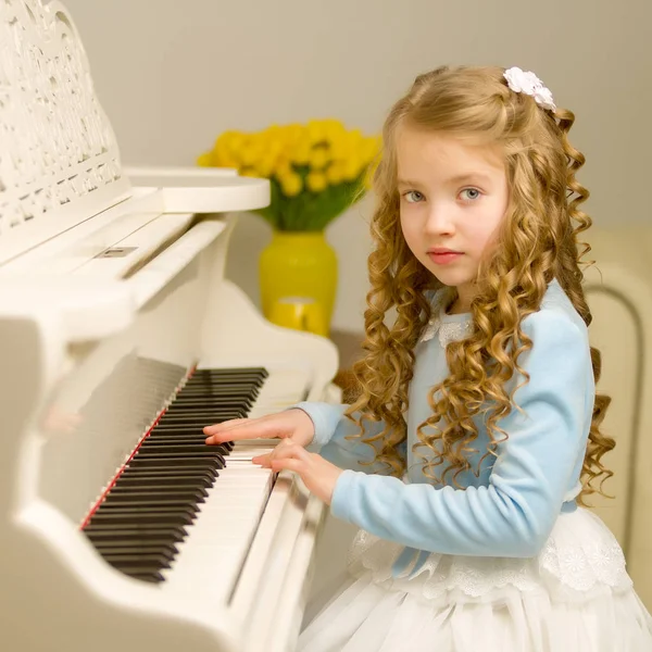 Menina bonita está tocando em um piano de cauda branco. — Fotografia de Stock