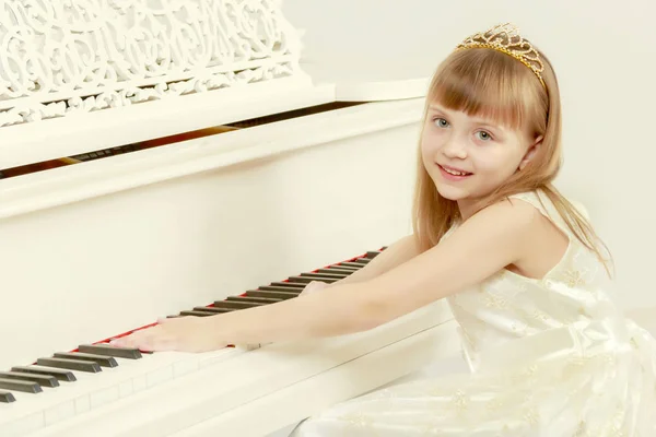 Uma menina está posando perto de um piano de cauda branco . — Fotografia de Stock