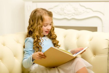 Küçük bir kız kanepede oturuyor ve kitap okuyor..