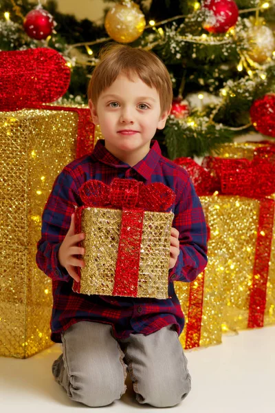 Een jongetje in de buurt van de kerstboom met een gift. — Stockfoto