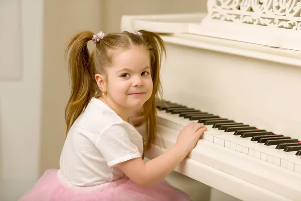 En vacker liten flicka spelar på en vit flygel. — Stockfoto