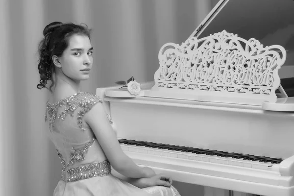 Uma adolescente está tocando em um piano de cauda branco . — Fotografia de Stock