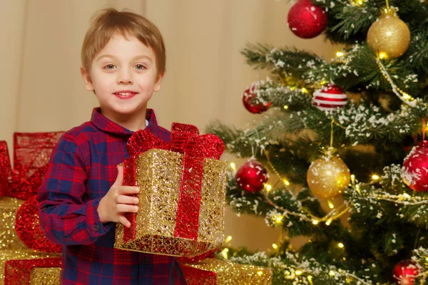 Een jongetje in de buurt van de kerstboom met een gift. — Stockfoto