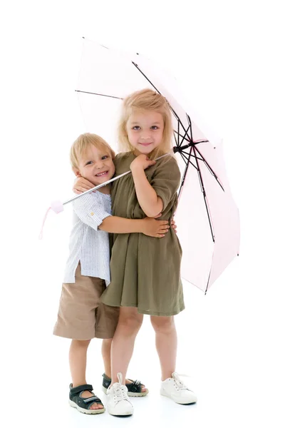 Uma rapariga e um rapaz, irmão e irmã escondidos da chuva debaixo de um... — Fotografia de Stock