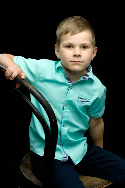 Petit garçon souriant assis sur un tabouret, sur un fond noir . — Photo