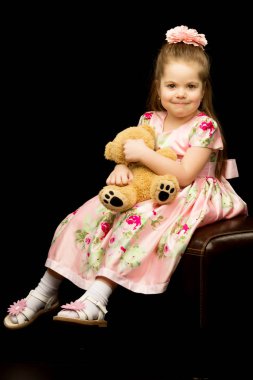 Siyah arka planda oyuncak ayısı olan küçük bir kız..