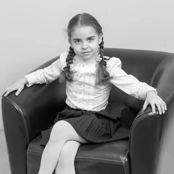 Een klein meisje zit op een stoel. Een lieve blonde met lange wated — Stockfoto