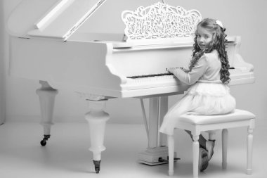 Güzel küçük kız beyaz bir piyanoda çalıyor..