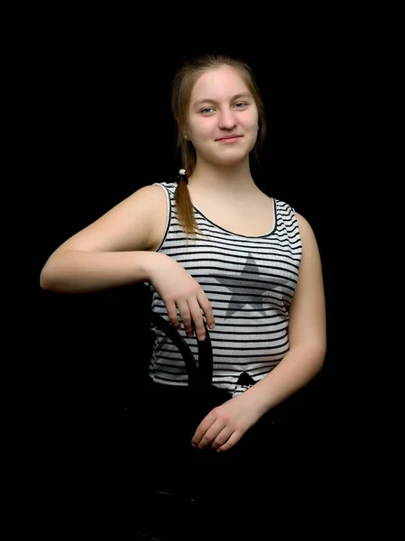 Charming girl teenager sitting on a chair in the studio on a bla — Stock Photo, Image