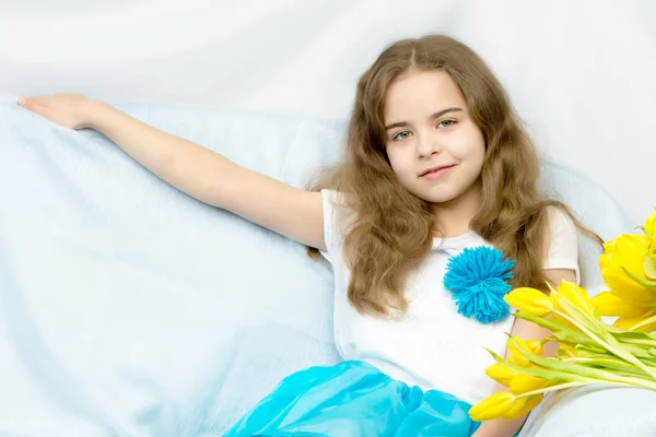 Mooie blonde schoolmeisje met gele tulpen zittend op de cou — Stockfoto