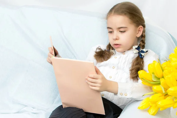 A diligent schoolgirl student with yellow tulips is sitting on t — Stock Photo, Image