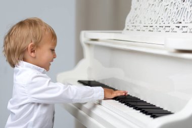 Studio beyaz piyano yakınındaki küçük çocuk.