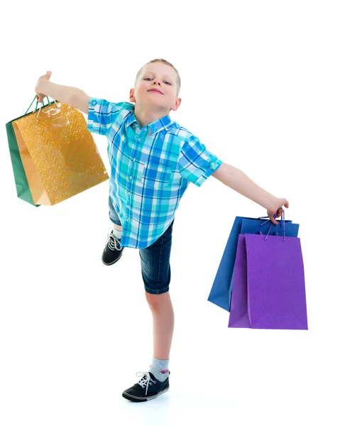 Rapaz a acenar sacos de papel multicoloridos. Ele vai às compras. — Fotografia de Stock