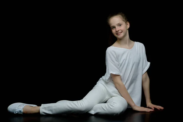 Una bambina si inginocchia su uno sfondo nero nello studio. — Foto Stock