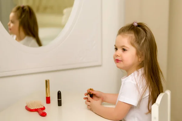 Uma menina perto do espelho pinta lábios de batom — Fotografia de Stock