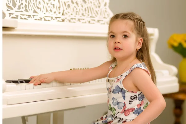 Menina bonita está tocando em um piano de cauda branco. — Fotografia de Stock