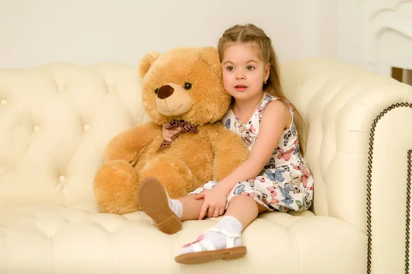 Little girl on sofa hugging teddy bear. — Stock Photo, Image