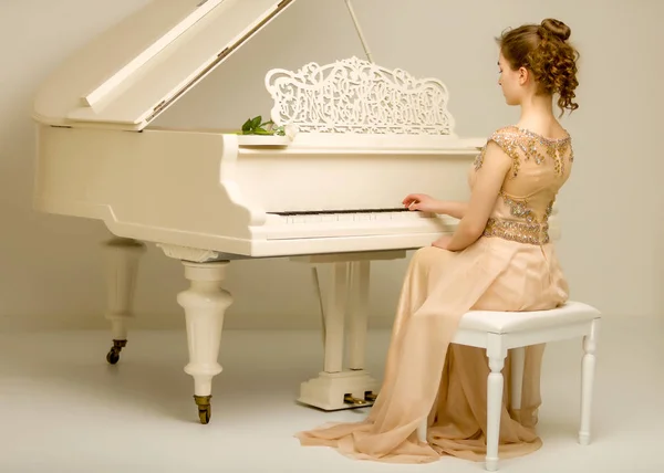 Uma adolescente está tocando em um piano de cauda branco . — Fotografia de Stock