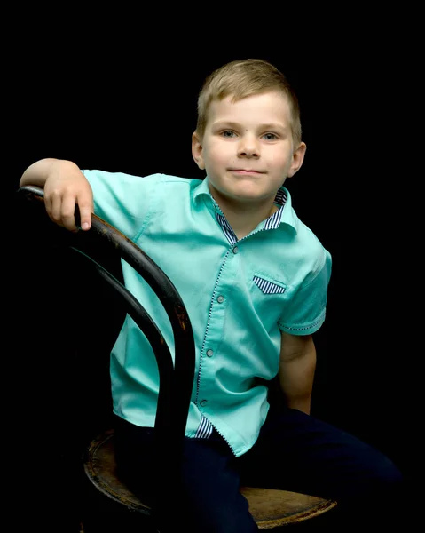 Glimlachend jongetje zittend op kruk, op een zwarte achtergrond. — Stockfoto