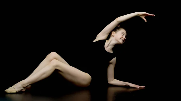Dziewczyna gimnastyczka w studio na czarnym tle wykonuje gimnastykę — Zdjęcie stockowe