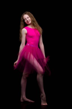 Stüdyodaki kız jimnastikçi siyah arka planda jimnastik yapıyor.