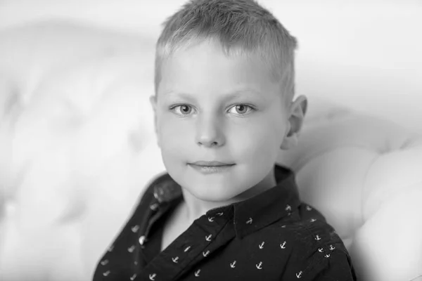 Un niño pequeño está sentado en el estudio en un sofá blanco. El cono — Foto de Stock