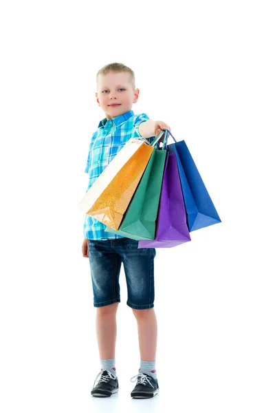 Rapaz a acenar sacos de papel multicoloridos. Ele vai às compras. — Fotografia de Stock