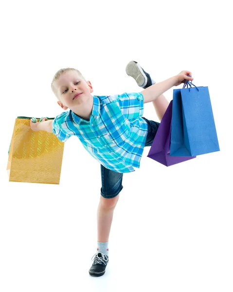 Маленький мальчик размахивает разноцветными бумажными пакетами. Он ходит по магазинам — стоковое фото