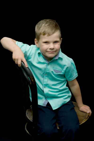 Petit garçon souriant assis sur un tabouret, sur un fond noir . — Photo