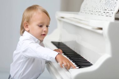 Studio beyaz piyano yakınındaki küçük çocuk.