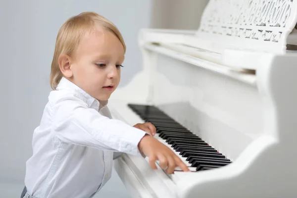 Kleiner Junge im Atelier neben weißem Klavier. — Stockfoto