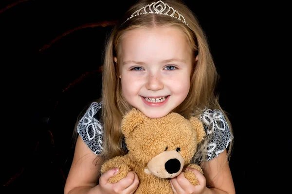 Klein meisje met een teddybeer op een zwarte achtergrond. — Stockfoto