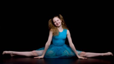 Stüdyodaki kız jimnastikçi siyah arka planda jimnastik yapıyor.