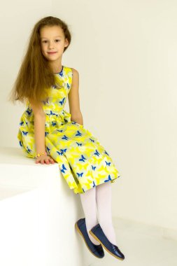 Küçük kız stüdyoda beyaz bir küple dergi için poz veriyor..